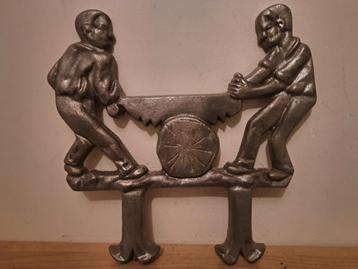 Pièce métallique représentant deux hommes utilisant une gran beschikbaar voor biedingen