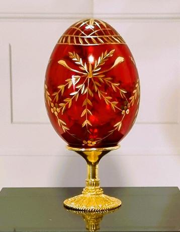Oeuf en cristal avec décorations dorées et base dorée.