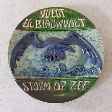 Rond wandbord in keramiek, vliegt de blauwvoet storm op zee