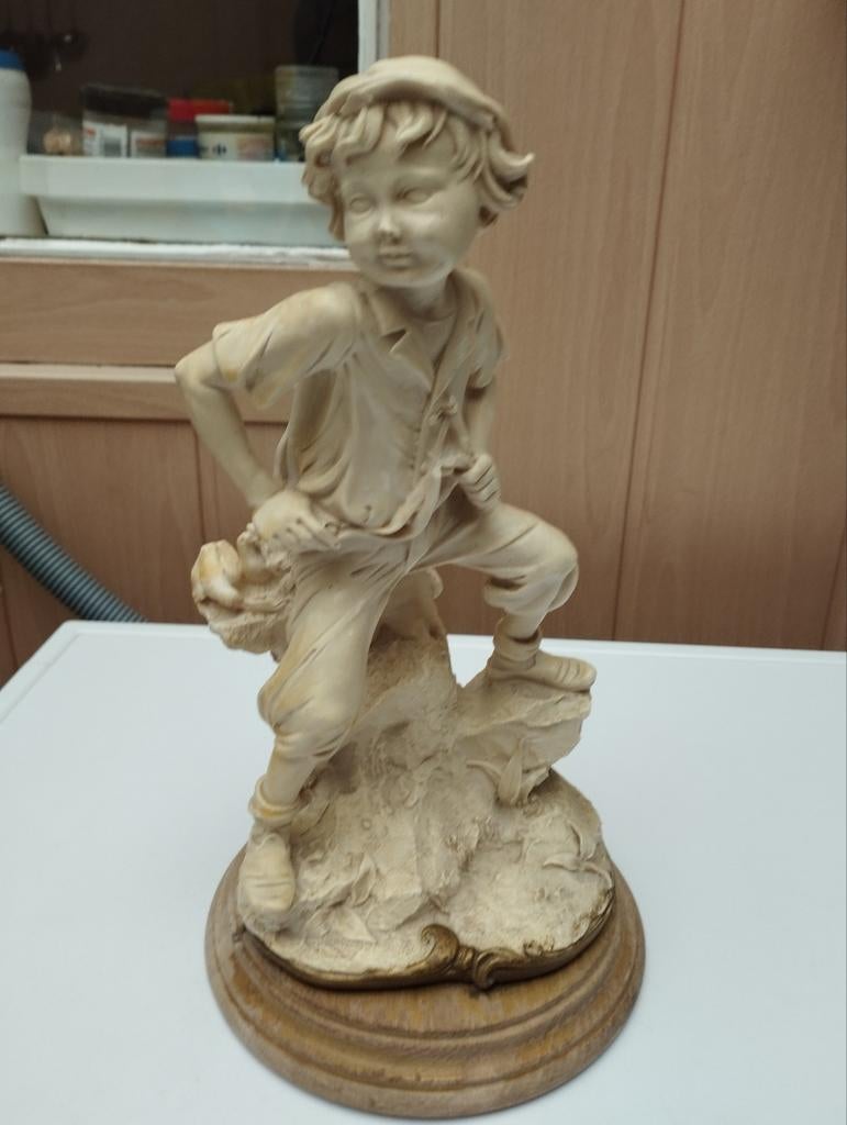 Een beeldje een jonge man die op een boomstam zit kleur vuil, Ophalen